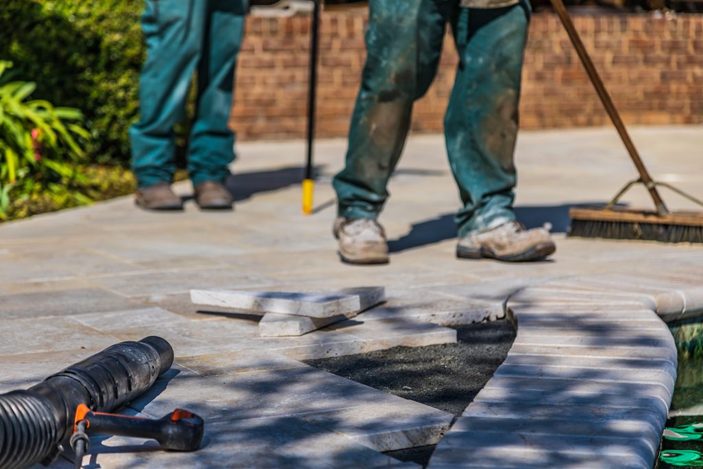 Pool installation work in progress with paving slabs removed beside the pool edge and construction tools on the surrounding deck.