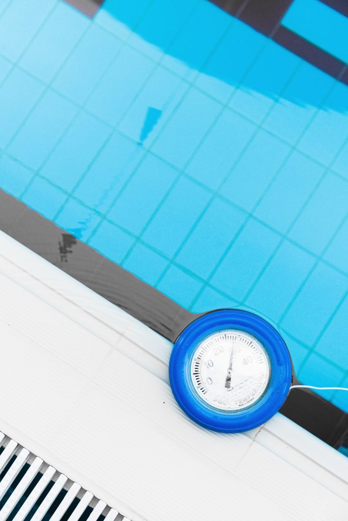 Floating pool thermometer placed on the edge of a tiled swimming pool, showing water temperature during pool maintenance checks.